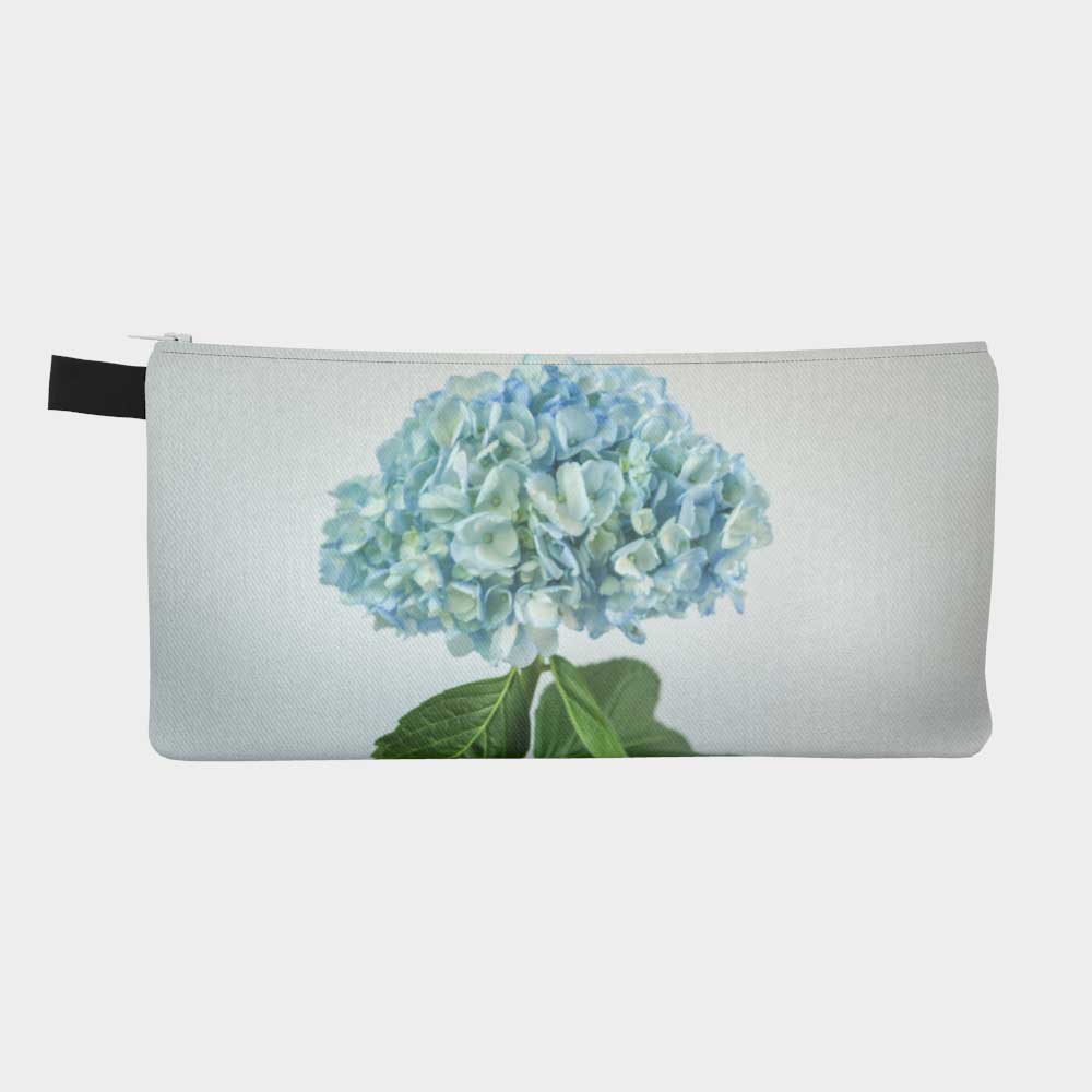 Close-up of zippered pouch with one single blue hydrangea flower and green foliage.